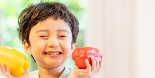 小さい男の子が野菜を持って無邪気に笑っている写真